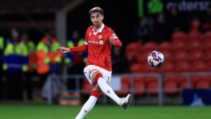 Lewis Brunt passando a bola com a camisa vermelha do Wrexham no Racecourse Ground